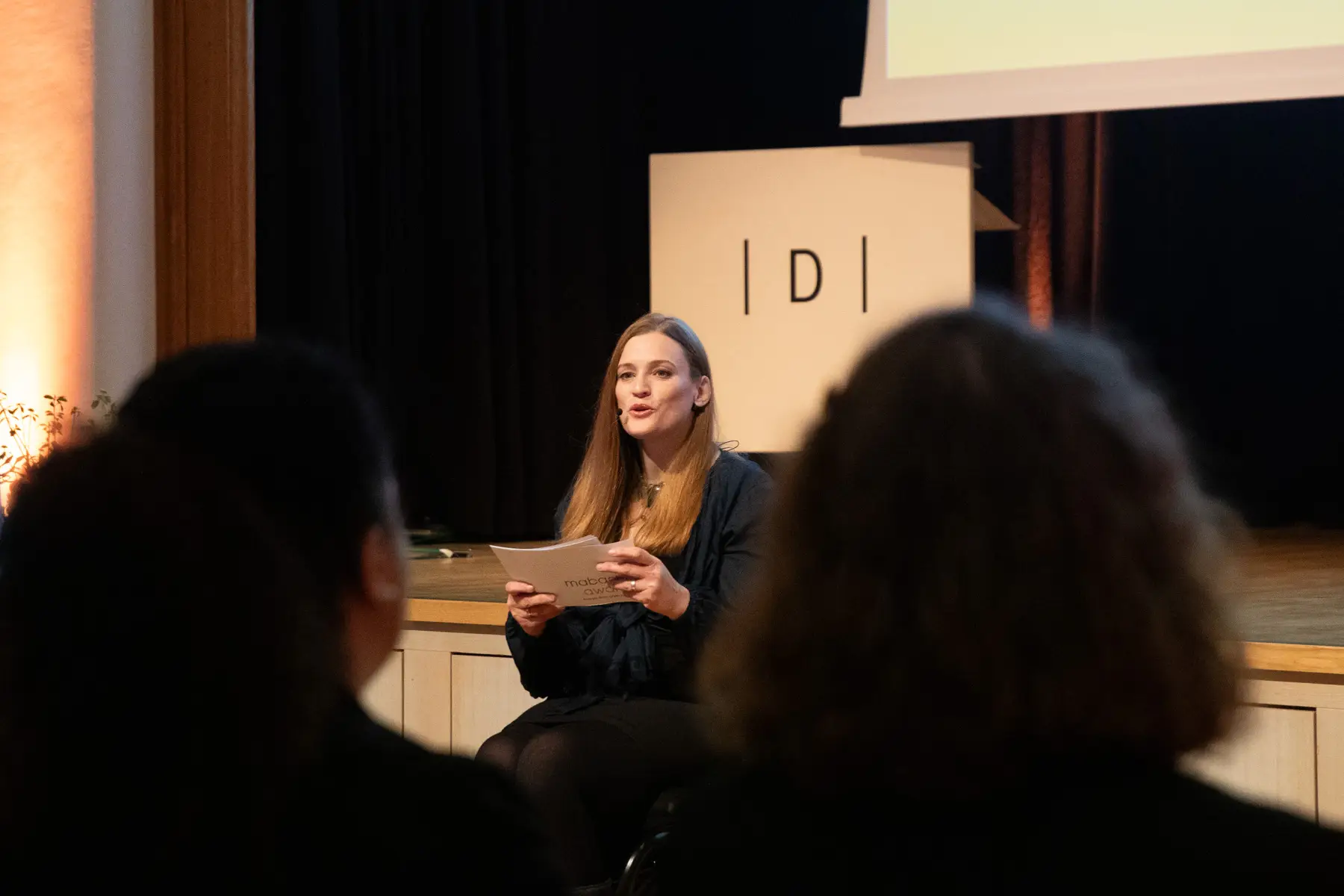 Moderatorin Barbara Sima-Ruml h&auml;lt Moderationskarten in der Hand und spricht zum Publikum